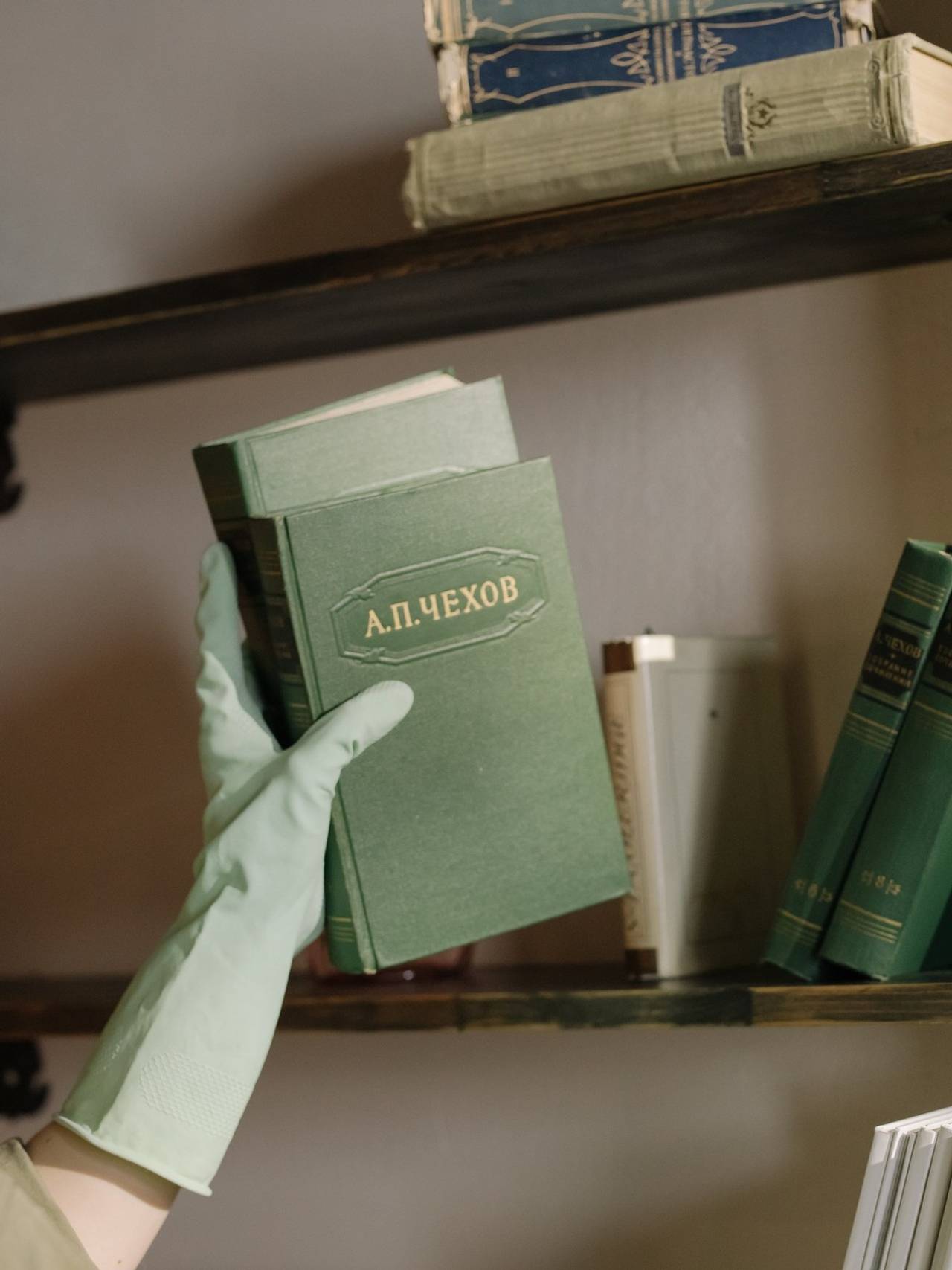 Mão com luva verde segurando dois livros de capa verde e colocando eles numa estante no sentido vertical
