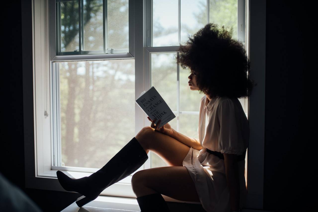 mulher sentada na janela lendo um livro